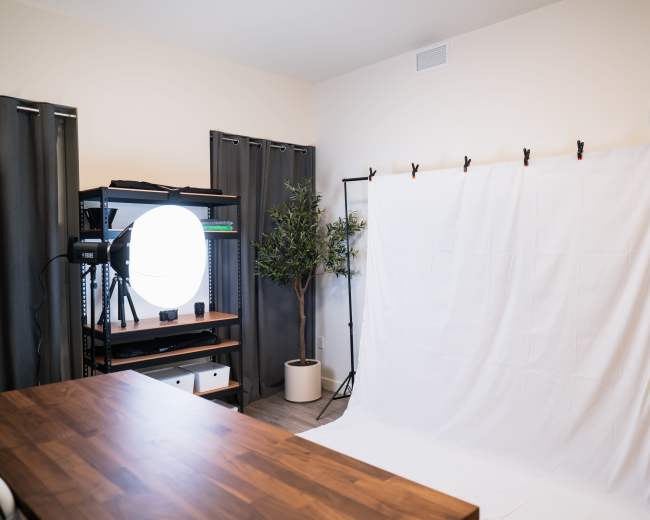 A photography studio setup with a white backdrop, a lighting setup, and a wooden table in a well-lit room.