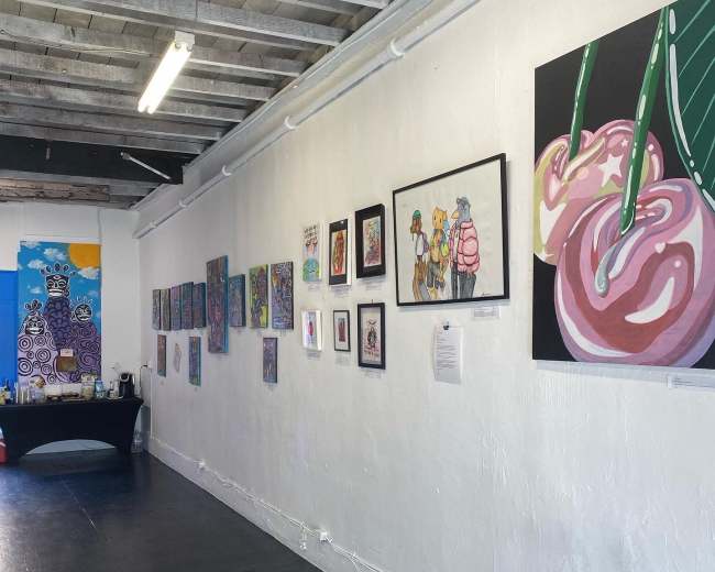 An art gallery with a white wall displaying various colorful paintings and a table in the foreground.