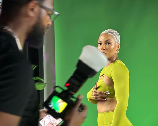 A model in a bright green outfit poses in front of a green screen while a photographer captures the shot.