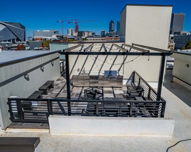 The image shows a rooftop patio with an outdoor kitchen and seating area, surrounded by a city skyline.