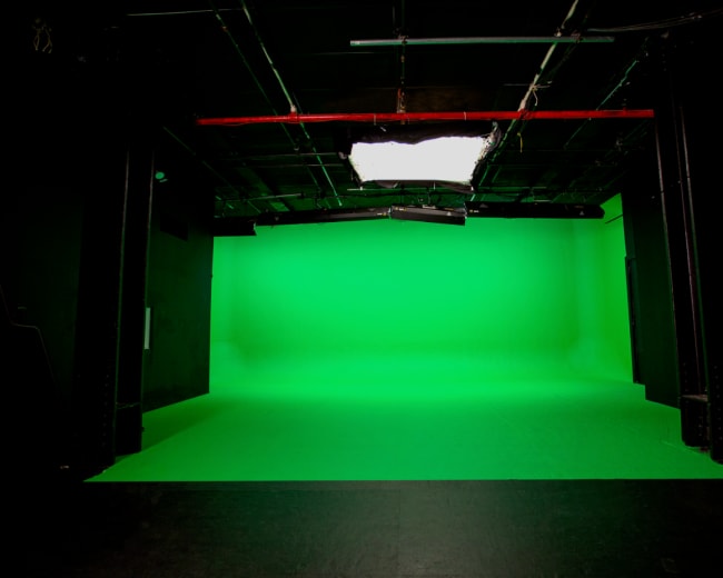 The image shows an empty studio with a bright green backdrop and dim overhead lighting.