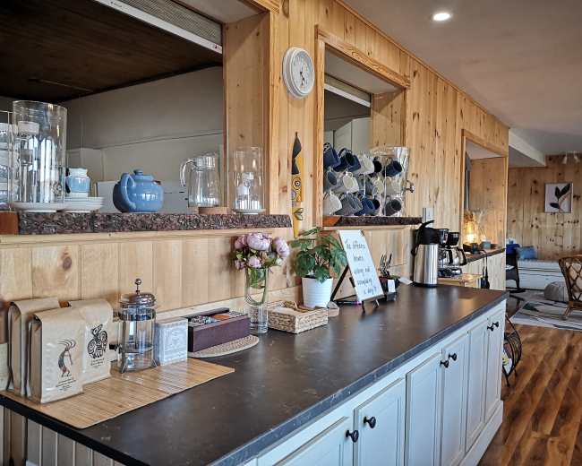 The scene features a wooden-paneled cafe setup with a counter displaying various glassware, a coffee maker, and a floral arrangement.