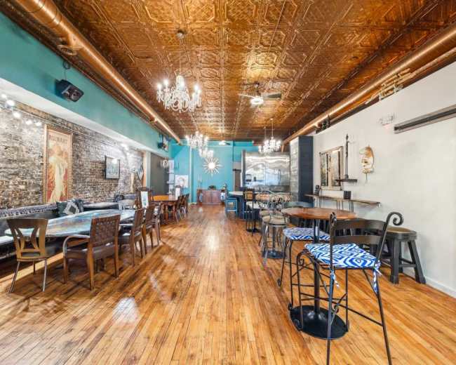 The image shows a stylish interior of a restaurant or bar with wooden floors, exposed brick walls, and decorative lighting fixtures.