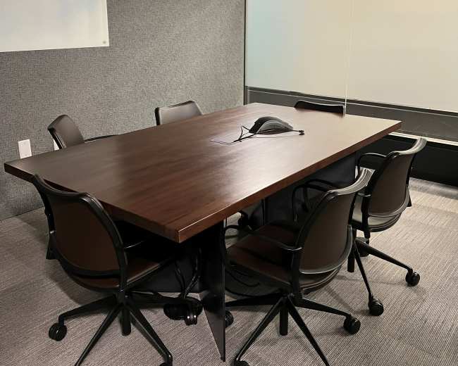 A large wooden conference table is surrounded by six black rolling chairs in a modern meeting room.