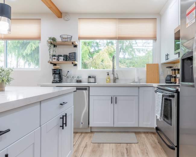 A modern kitchen with white cabinetry, stainless steel appliances, and a window offering a view of greenery outside.