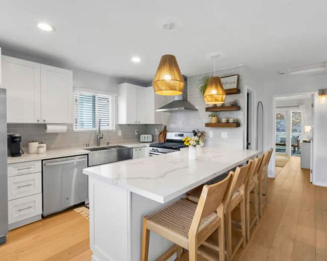 A modern kitchen features white cabinetry, stainless steel appliances, and a large island with pendant lighting and bar stools.