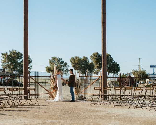A couple stands at an altar surrounded by empty rows of chairs in an outdoor wedding venue.