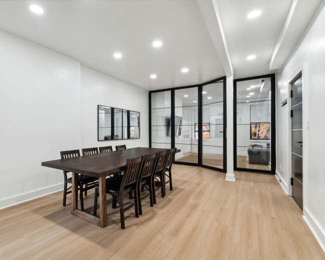 A spacious dining area features a large table surrounded by wooden chairs, with glass partitions leading to another room.