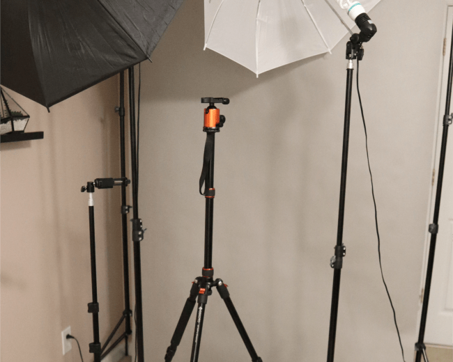 A photography setup featuring three light stands, two with reflective umbrellas and one with a softbox, positioned in front of a gray backdrop.