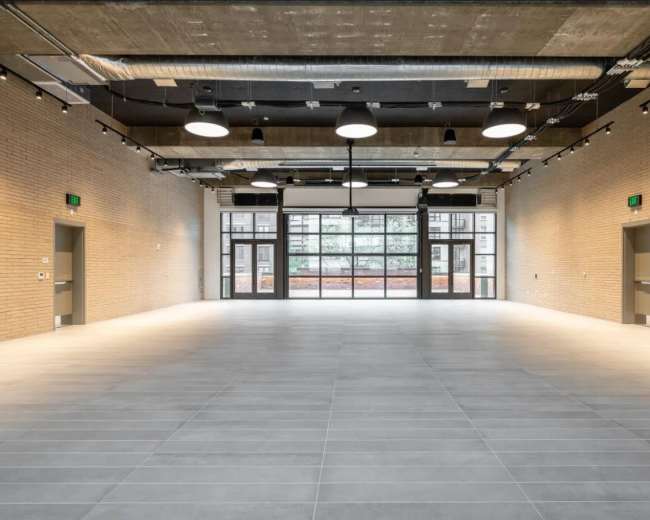 The image shows a spacious, modern interior with light-colored brick walls, large windows, and a tiled floor.