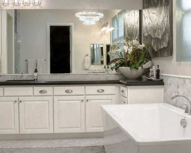A well-lit bathroom features a large bathtub, dual sinks with a dark countertop, and decorative potted plants on a stylish vanity.
