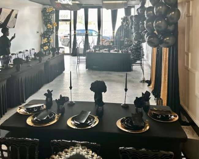 A banquet hall elegantly decorated in black and gold, with tables set for a formal event and decorative balloons along the walls.