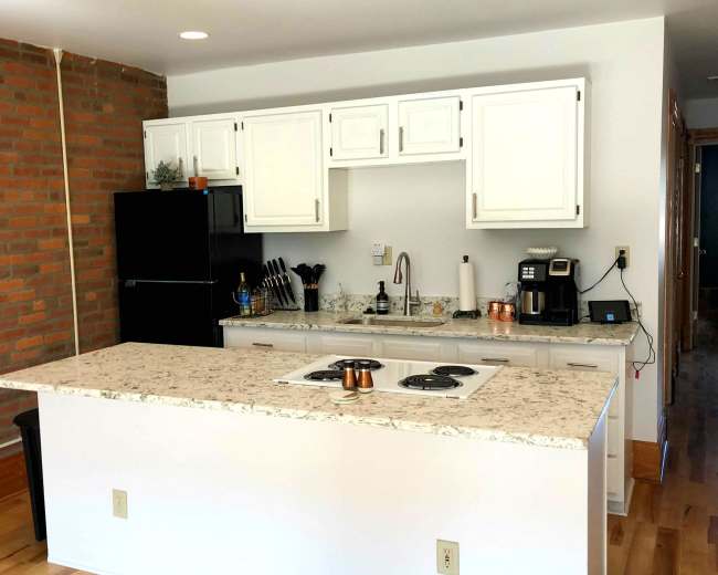 The image shows a modern kitchen with white cabinetry, a black refrigerator, and a kitchen island featuring a stovetop.