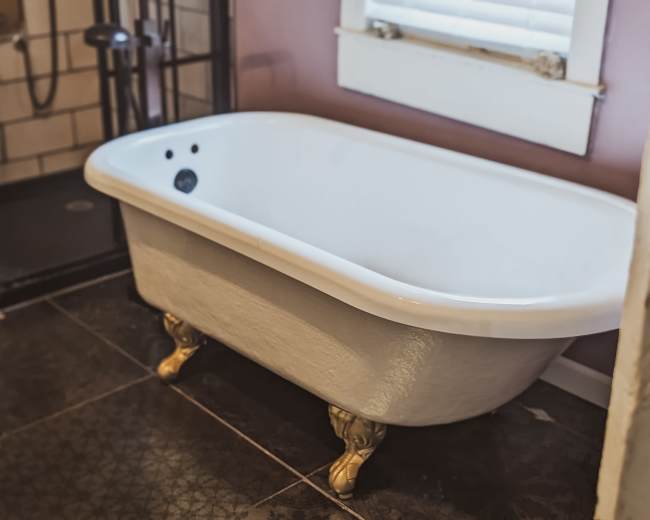 A vintage clawfoot bathtub beside a glass shower enclosure in a bathroom with dark tiled flooring.