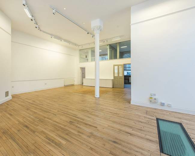 A spacious, empty room with wooden flooring, white walls, and large windows.