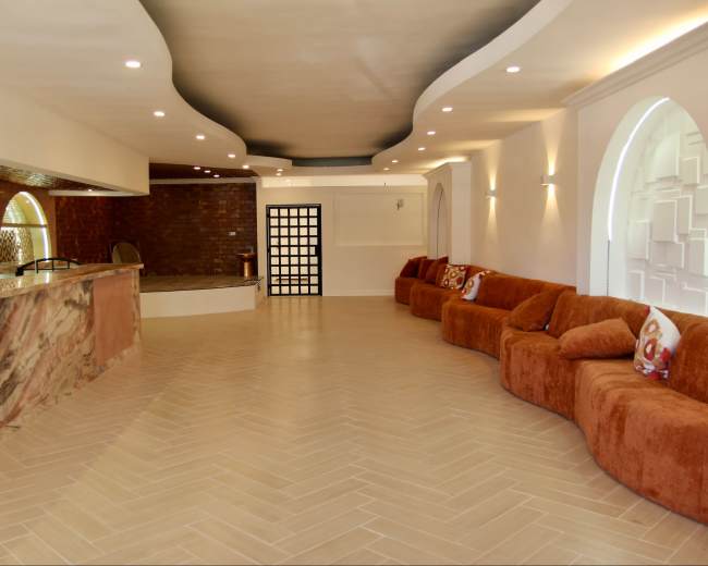 The image shows a spacious, modern interior featuring a curved sofa, a bar area with stone countertops, and decorative wall elements.