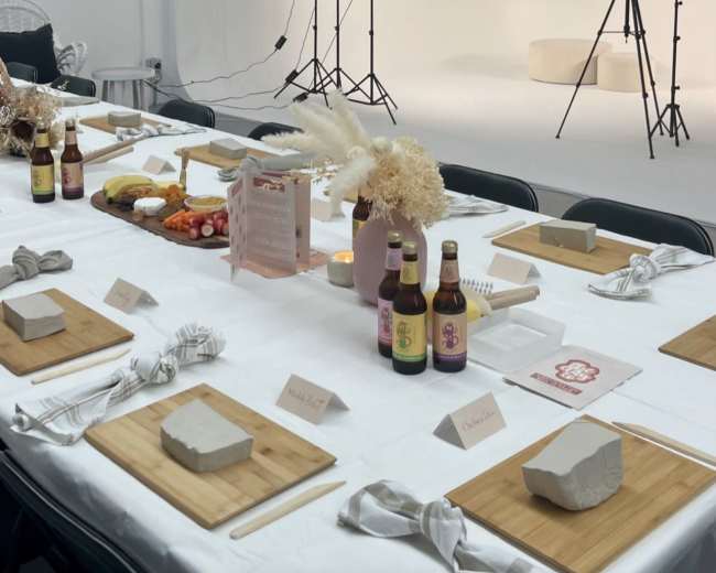 A table is set with various food items and drinks, with a photography backdrop and lighting equipment in the background.