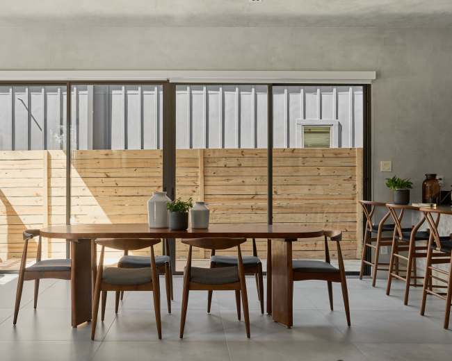 A modern dining area features a wooden table surrounded by chairs, with large sliding glass doors that open to a fenced outdoor space.