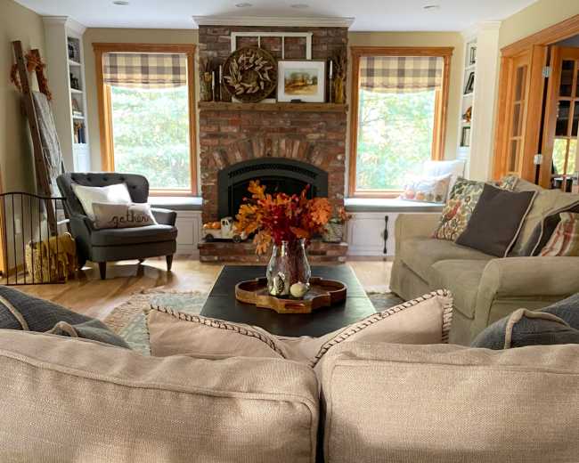 The image shows a cozy living room featuring a stone fireplace, comfortable seating arrangements, and a coffee table adorned with decorative items and flowers.