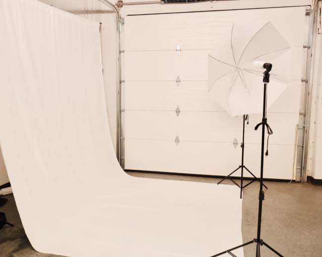 The image shows a photography studio with a white backdrop and a softbox lighting setup against a garage door.