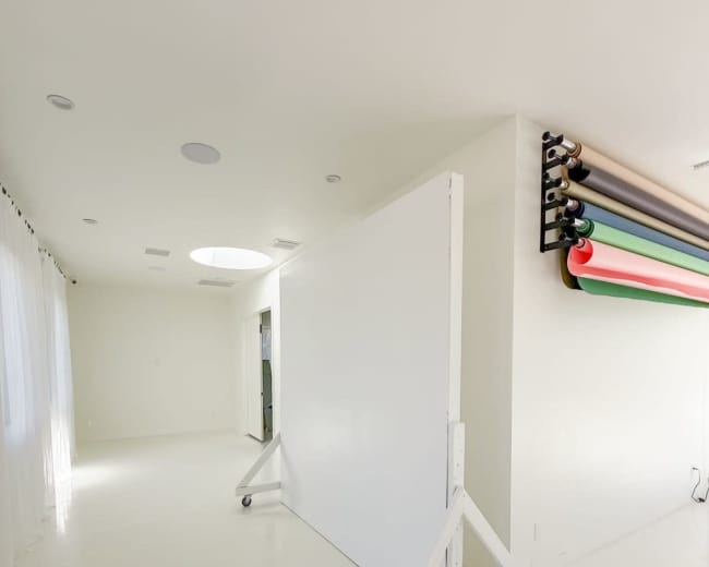 The image shows a spacious room with a movable white backdrop on wheels and assorted rolls of colored paper mounted on the wall.