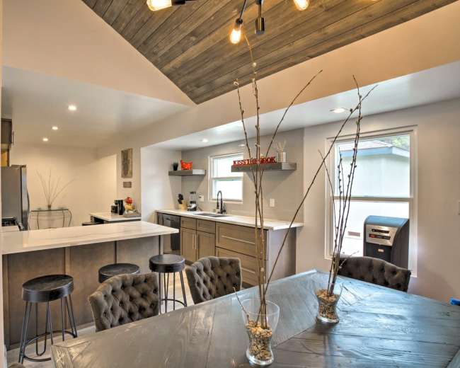 A modern kitchen and dining area featuring a white countertop, dark cabinetry, and a wooden ceiling with exposed lighting.