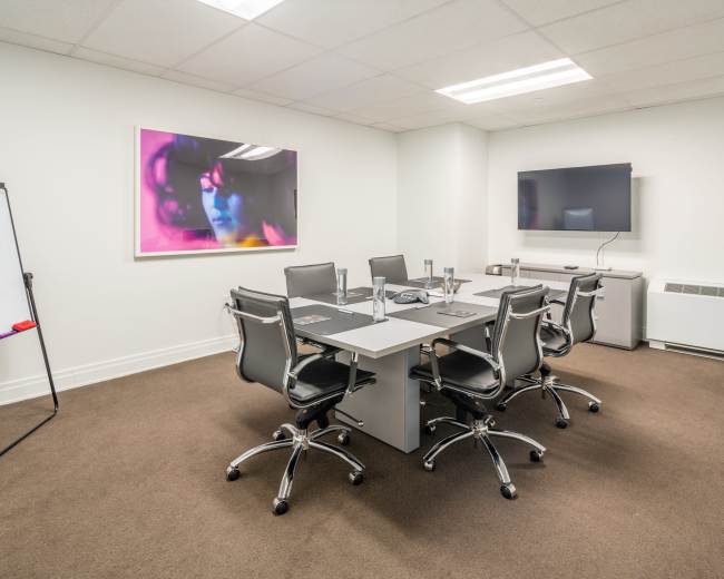 A modern conference room with a rectangular table surrounded by six chairs, a whiteboard, and a television mounted on the wall.
