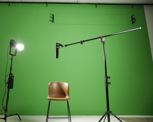 A brown chair is positioned in front of a green backdrop, with a spotlight and a microphone setup on either side.