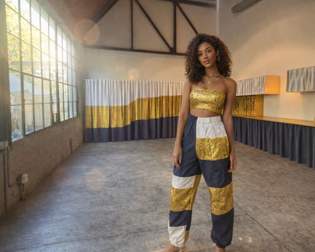 A woman with curly hair stands in a spacious, well-lit studio featuring large windows and decorative fabric panels.