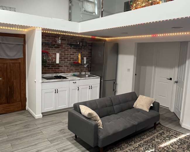 A modern living space features a gray sofa, a kitchen with white cabinets, and a glass-railed loft area decorated with a Christmas tree.