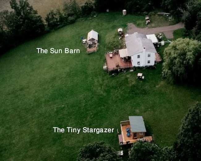 A large grassy area with a white house, a deck, and two smaller buildings labeled "The Sun Barn" and "The Tiny Stargazer."