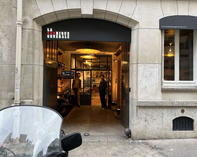 The entrance of a boutique named "La Fabrique Générale" is visible, showcasing a modern interior with customers inside and a motorcycle parked in front.