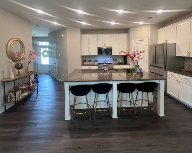 The image shows a modern kitchen with a central island, bar stools, and white cabinets, featuring a bright and open layout.