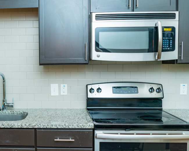 The image shows a kitchen with dark cabinets, a stainless steel microwave above a black stove, and a granite countertop with a sink.