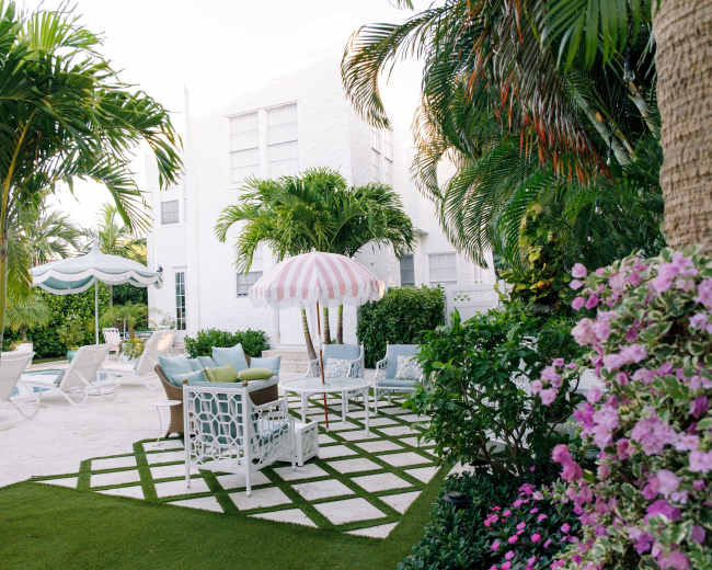 The image shows a landscaped outdoor area with a pool, lounge chairs, and a pink-striped umbrella surrounded by greenery and flowers.