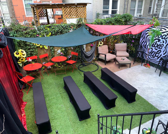 A small outdoor venue with green grass, red and green canopies, seating areas, and decorated walls, ready for an event.
