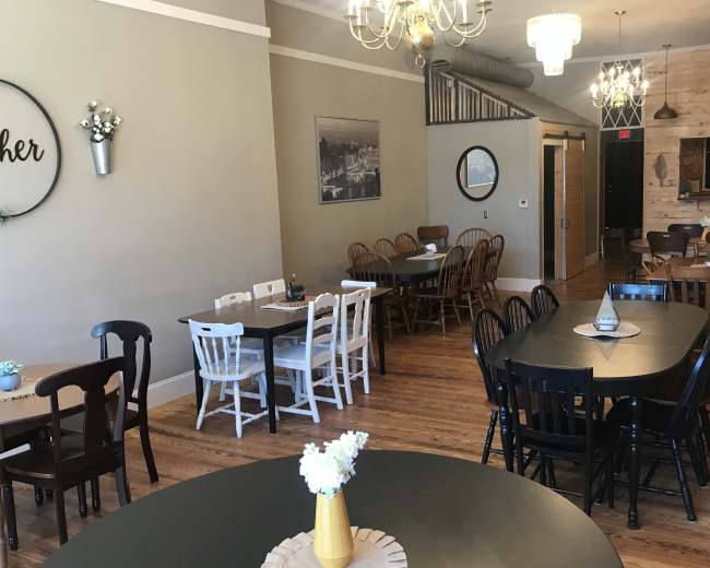 The image shows a spacious dining area with various tables and chairs arranged around the room, featuring a mix of light and dark wood finishes.