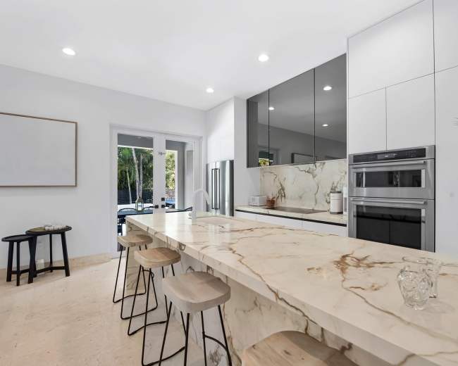 The kitchen features a marble countertop with bar seating, glass-front cabinets, and modern appliances.