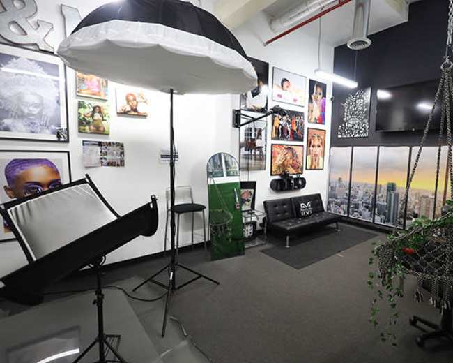 The image shows a photography studio featuring various framed portraits on the walls, a swing chair decorated with plants, and professional lighting equipment set up for shoots.