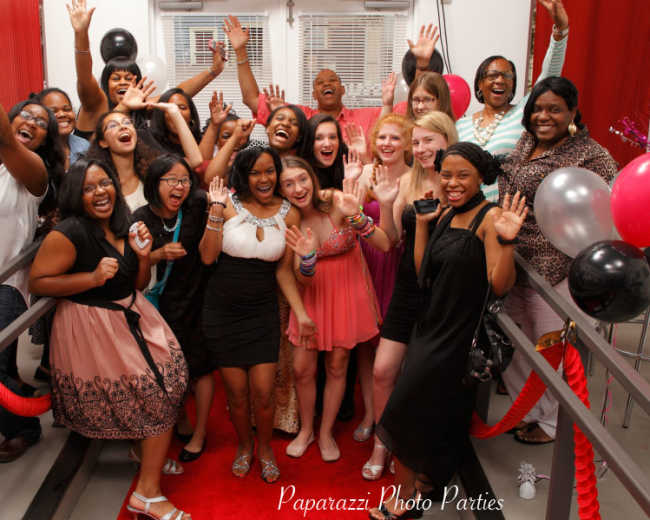 A large group of young women and girls are gathered together, smiling and posing enthusiastically for a photo in a decorated party setting.