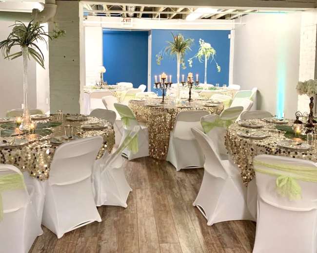 The image shows a decorated event space with elegantly arranged tables covered in sequin tablecloths, adorned with candles and centerpieces.