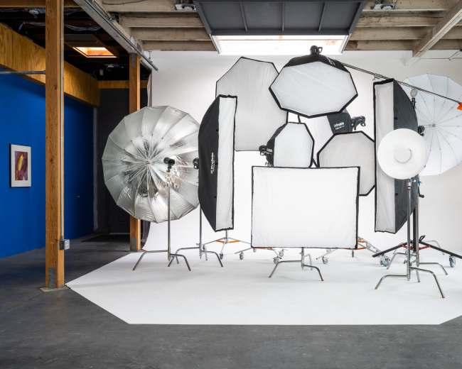 A photography studio setup featuring various lighting equipment, including softboxes and reflectors, arranged against a white backdrop.