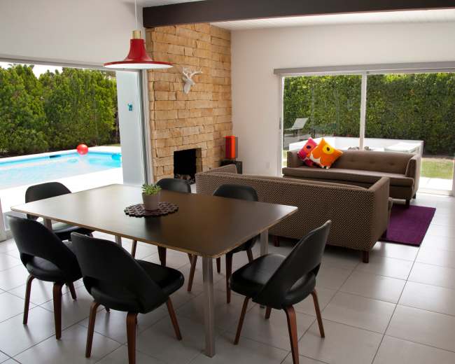 A modern living room and dining area with a view of a pool and greenery outside.