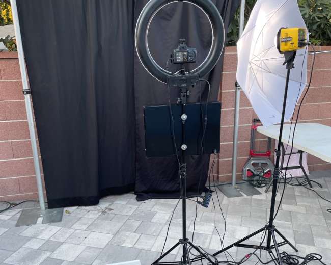 The image shows a photography setup with a ring light, an umbrella softbox, a camera on a tripod, and a backdrop in an outdoor area.