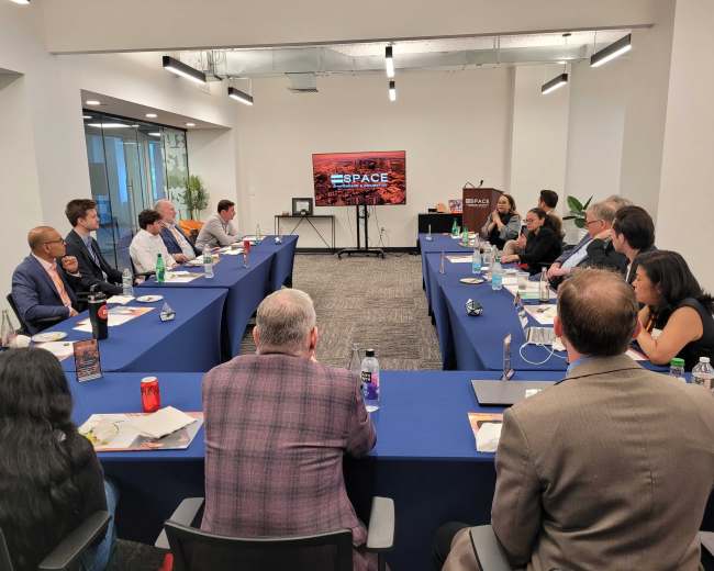 A group of people sits around a long conference table in a meeting room, with a screen displaying the word "SPACE" at the front.