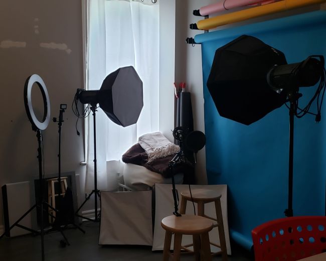 A photography setup in a room with lighting equipment, a backdrop, and a few chairs arranged near a window.