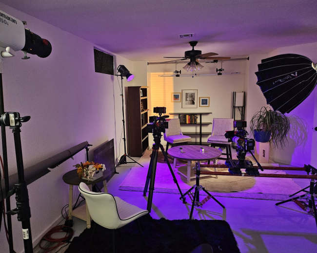 A well-equipped studio setup features various lighting fixtures, cameras, and a small table in a modern living space.