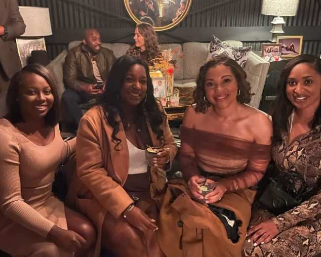 A long banquet table is set outdoors with elegant decor, surrounded by greenery and string lights.