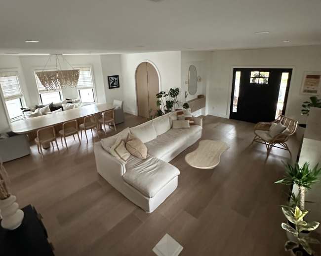 The image shows a spacious living room with a large sectional sofa, a coffee table, and a dining area with a visible kitchen in the background.