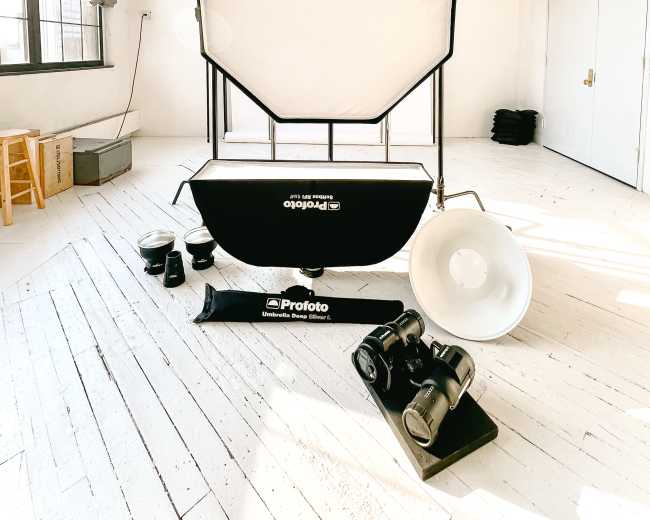 The image shows a photography setup in a bright studio, featuring an octagonal softbox, various camera lights, and a backdrop.